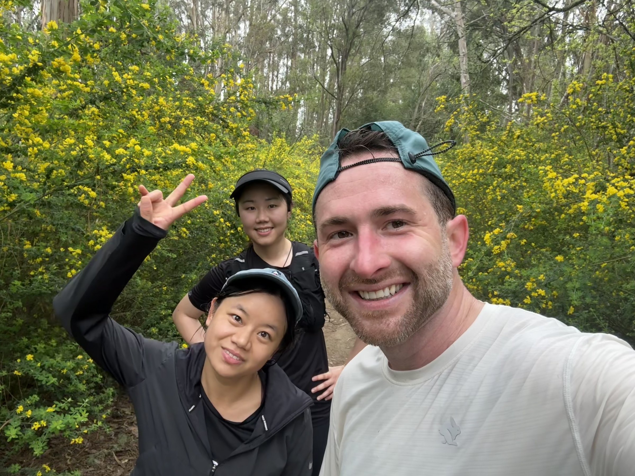 Three members smiling on a Tilden Park trail run surrounded by yellow wildflowers